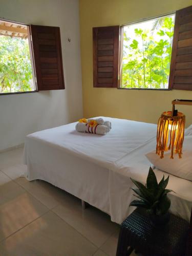 a bedroom with a bed with white sheets and two windows at Villa dos Coqueirais in Icaraí