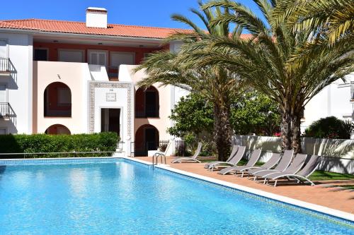 a pool with chairs and palm trees in front of a building at T3 terraço e piscina Praia del Rey Óbidos C14 in Amoreira