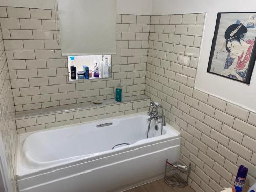 a bathroom with a tub and a white tiled wall at Kilmactrasna Cottage in Carrickmacross