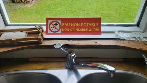 a sink in a kitchen with a sign on a window at La maison du capitaine est à vous! in Tadoussac