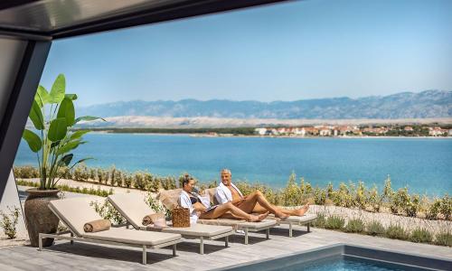 two people sitting on a couch next to a swimming pool at Aminess Style Glamping Villas & Holiday Homes Avalona in Povljana