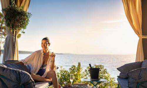 a woman sitting on a couch in front of the ocean at Aminess Style Glamping Villas & Holiday Homes Avalona in Povljana
