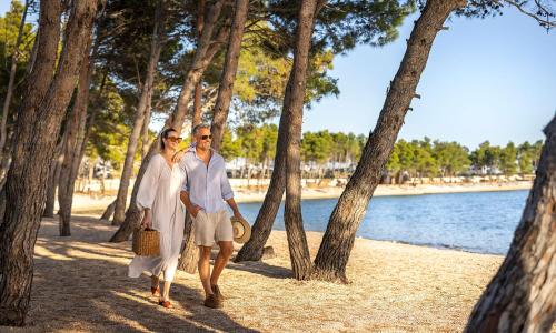 a man and woman walking along a beach with trees at Aminess Style Glamping Villas & Holiday Homes Avalona in Povljana
