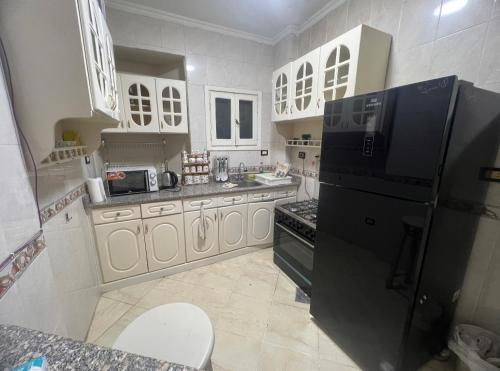 eine Küche mit einem schwarzen Kühlschrank und weißen Schränken in der Unterkunft Happy home in Hurghada