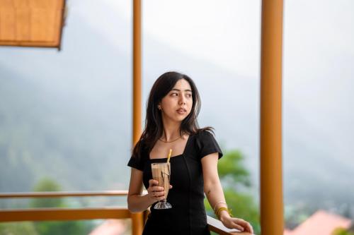 a woman in a black dress holding a drink at Olgah Manali in Manāli