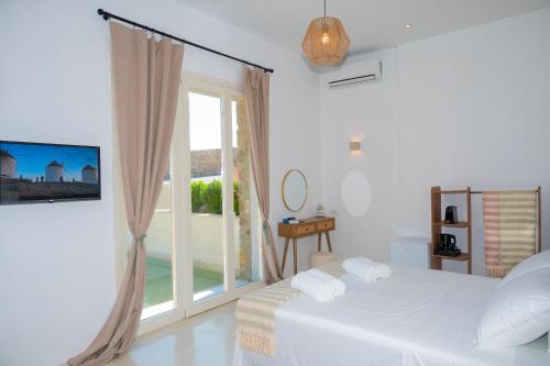 a white bedroom with a bed and a large window at Adyton Mykonos Luxury Suites & Pools in Ano Mera