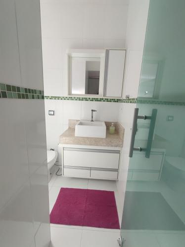 a white bathroom with a sink and a mirror at Casa com garagem, ar condicionado, sala tv e jantar, cozinha completa e lavanderia in Taubaté
