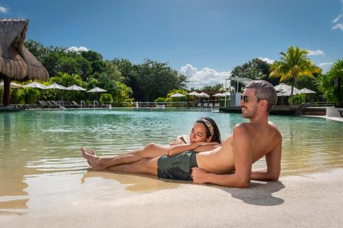 a man and woman sitting on the beach in the water at El Beso Adults Only at Ocean Riviera Paradise All Inclusive in Playa del Carmen