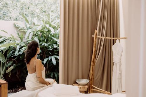 a woman sitting on a bed looking out a window at Elements Of Byron in Byron Bay