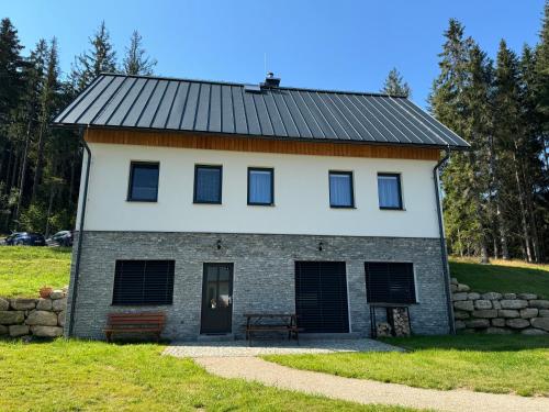 a house with a black roof and a stone wall at Apartmán U lesa in Smržovka