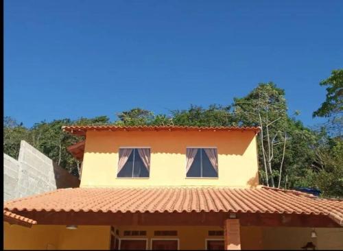 ein gelbes Haus mit einem roten Dach mit zwei Fenstern in der Unterkunft Chalé Vitória 1- Rancho dos 7 in Arapeí