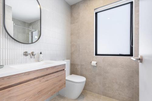 a bathroom with a sink and a toilet and a mirror at Modern 2BR Townhouse in Mission Bay I Zodiak Stays in Auckland