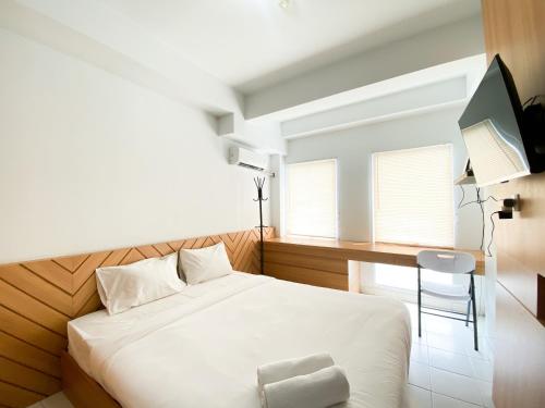 a bedroom with a white bed with a chair and window at Best Homey Studio at Patraland Urbano Apartment By Travelio in Bekasi