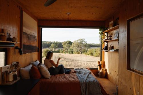 巴瑟尔顿Flynn the Tiny Cabin in Busselton的一位女士坐在床上，望着窗外