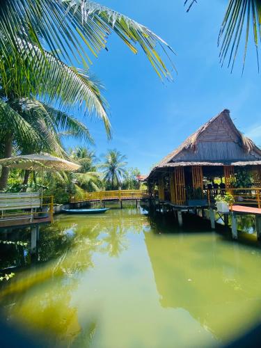 a river with a house and a bridge and palm trees at Alina Retreat in Hiếu Nhơn