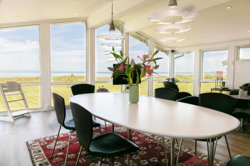 a dining room with a white table and chairs and windows at Strandhuset. in Asperup