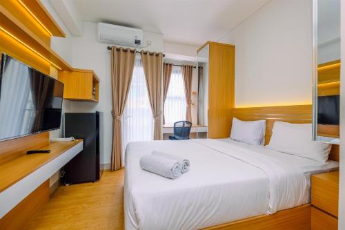 a bedroom with a large white bed and a television at Comfort and Best Deal Studio Room Transpark Cibubur Apartment By Travelio in Depok