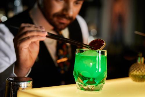 a man is stirring a green drink with a stick at The George Hamburg in Hamburg