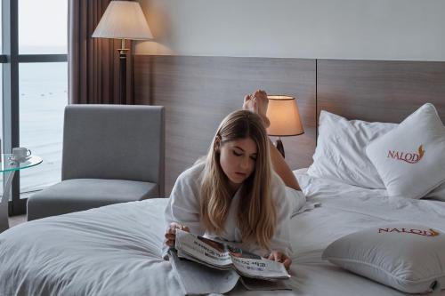 a girl sitting on a bed reading a magazine at The Nalod Da Nang in Da Nang
