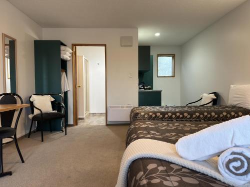 a bedroom with two beds and a desk and a table at ASURE Ambassador Motor Lodge in Oamaru