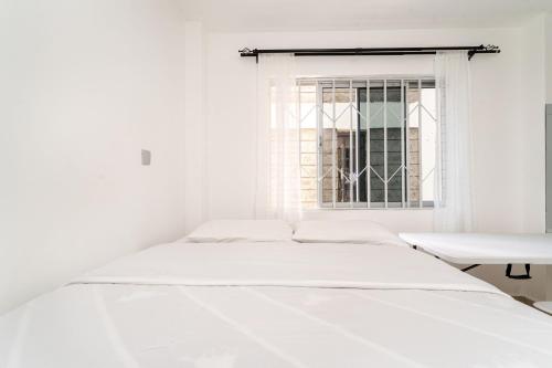 a white bedroom with a bed and a window at Beths serviced apartments in Ruiru