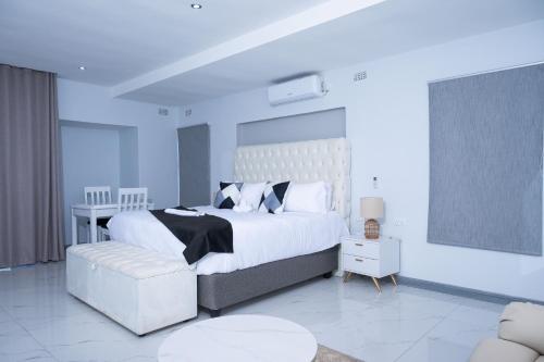 a white bedroom with a large bed and a chair at De Lux Villa in Bulawayo