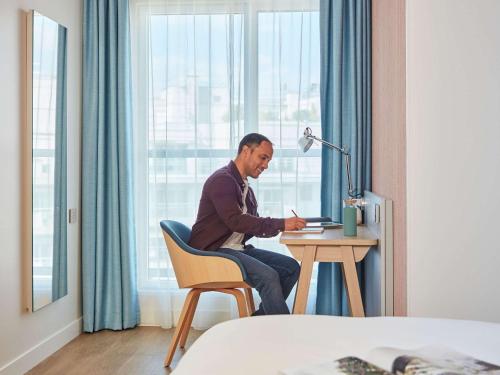 a man sitting at a table in a hotel room at Aparthotel Adagio Paris Boulogne in Boulogne-Billancourt