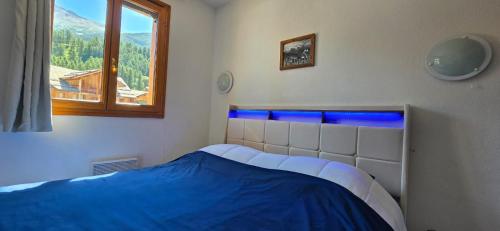 une chambre avec un lit avec une couverture bleue et une fenêtre dans l'établissement Cocon des Orres res balcon des airelles appartement 512, aux Orres