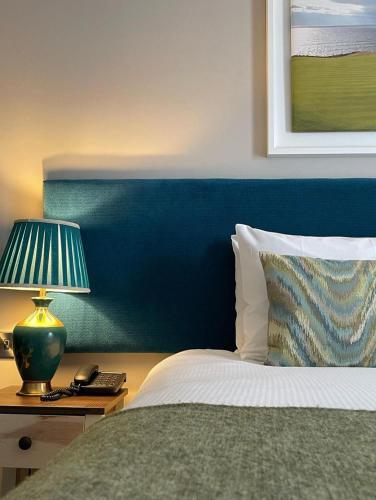 a bed with a blue headboard and a lamp on a table at Rooms at The Marine in Ballybunion