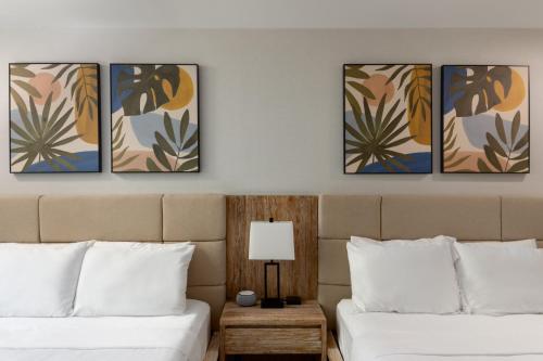 two beds in a hotel room with four paintings on the wall at The Wave at Marblehead in Marblehead