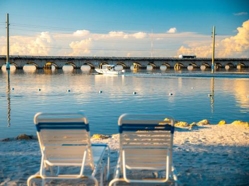 two chairs sitting on the beach near the water with a bridge at Sugarloaf Key Hotel at KOA Resort in Summerland Key