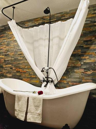 a white bath tub with a curtain on a brick wall at Private Cabin- Breakfast - Double Tub - 75in TV - SUP - Washer Dryer - BBQ in West Point