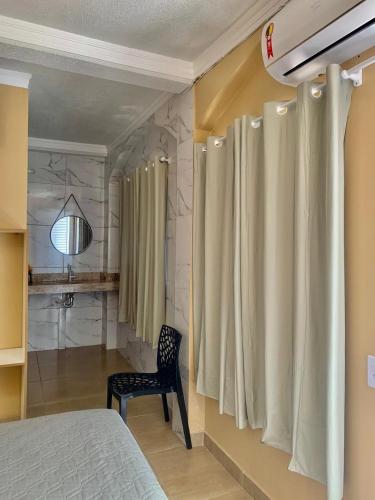 a bedroom with a bed and a chair and a shower curtain at Hotel Coqueiros in Valparaíso de Goiás