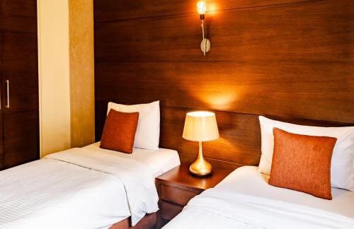 two beds in a room with wooden walls and a lamp at Britannia Suites in Beirut