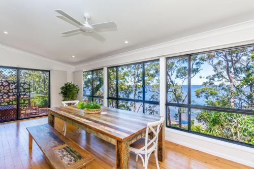 a dining room with a wooden table and large windows at The Observation Deck by Experience Jervis Bay in Sanctuary Point
