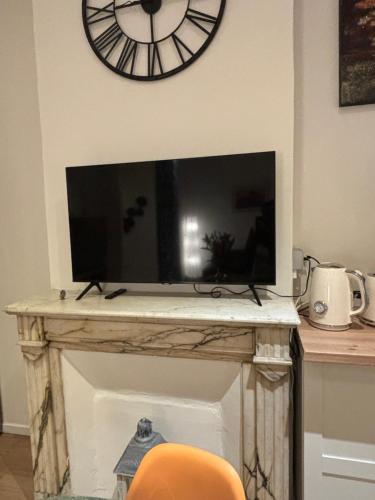 a tv on top of a fireplace with a clock on the wall at Astou Cisse in Marseille