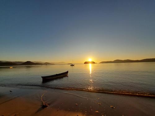 a boat on the beach with the sunset in the background at Pousada Lírios do Campo Hidromassagem - Sauna-Ar condicionado - Piscina - salão de jogos - 200 metros da praia Jabaquara in Paraty