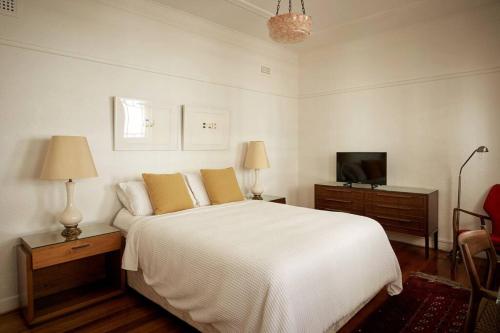 a white bedroom with a bed and a television at Boutique Art Deco Apt, Beach, Park, Shops, Cafes F1 in Melbourne