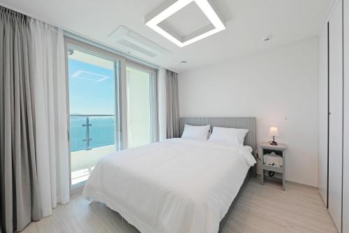 a white bedroom with a bed and a large window at Elmomento Songdo in Busan
