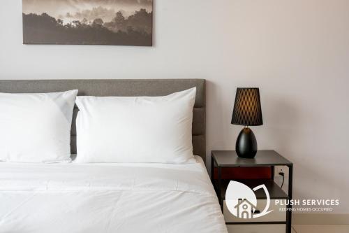 a bed with white sheets and a nightstand with a lamp at Gaia Residences by Plush in Rawang