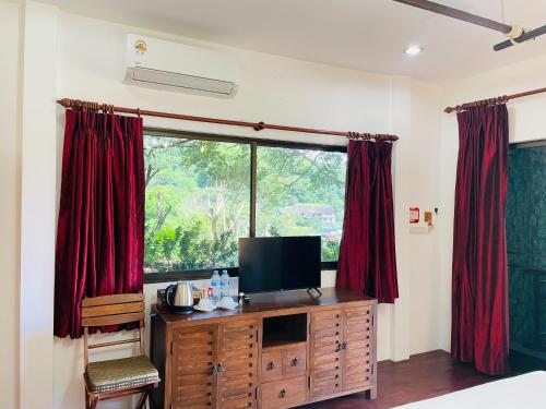 a bedroom with a tv and a window with red curtains at Boomerang Village Resort Kata in Kata Beach