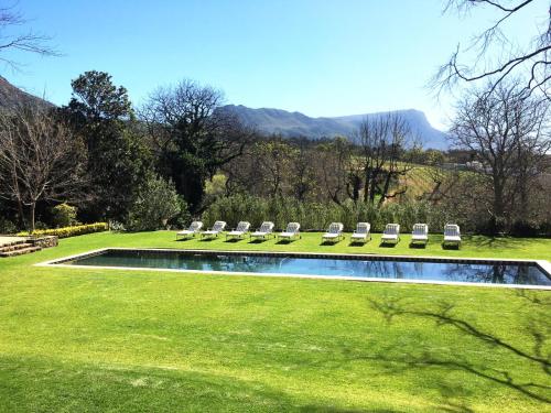 a group of lawn chairs and a pool with mountains in the background at Constantia Klein in Cape Town