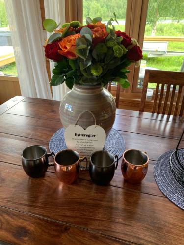 a vase with flowers and three cups on a table at Mitt paradis in Bardufoss