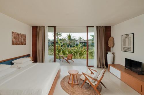 a bedroom with a bed and a tv and chairs at Origin Lombok in Kuta Lombok