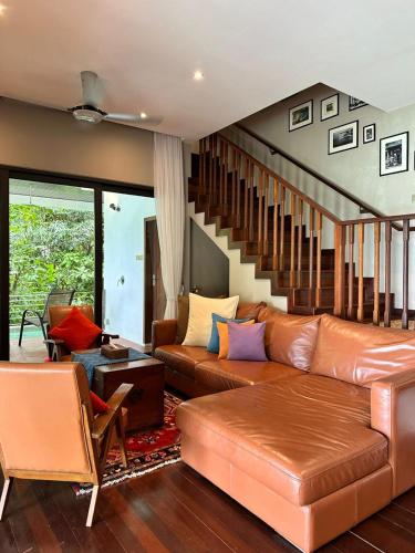 a living room with a brown leather couch and stairs at Ambong Pool Villas - Private Pool in Pantai Cenang