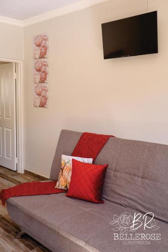 a gray couch with red pillows in a living room at Bellerose Guesthouse in Klerksdorp