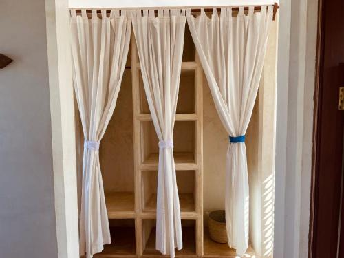 a room with white curtains and a book shelf at Swahili Dreams Apartments in Lamu