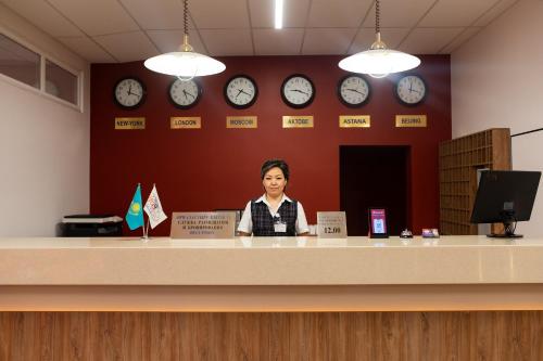 a woman sitting at a counter with clocks on the wall at Aktobe Hotel in Aktobe