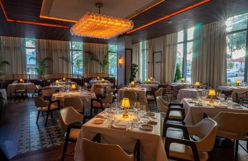 a restaurant with white tables and chairs and windows at The Ray Hotel Delray Beach, Curio Collection By Hilton in Delray Beach