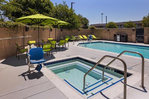 a swimming pool with chairs and a table and an umbrella at SpringHill Suites by Marriott Turlock in Turlock